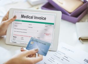 A medical invoice displayed on a tablet with a person holding a credit card, representing revenue cycle management in healthcare.